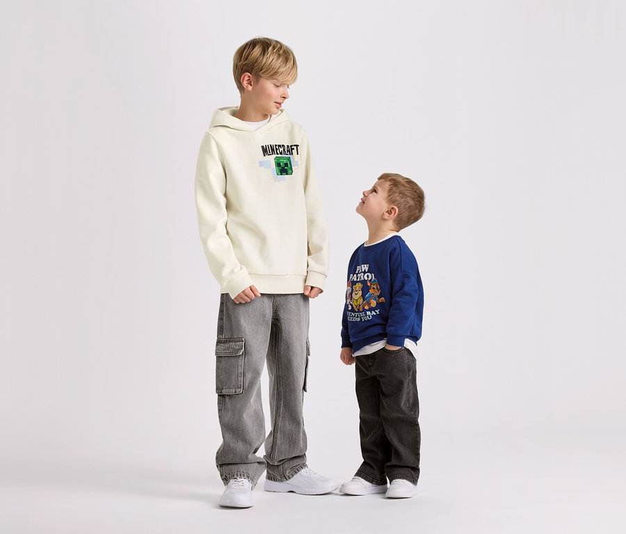 Két fiú áll fehér háttér előtt. A nagyobbik fiú egy MINECRAFT mintás kapucnis szabadidőfelsőt visel.