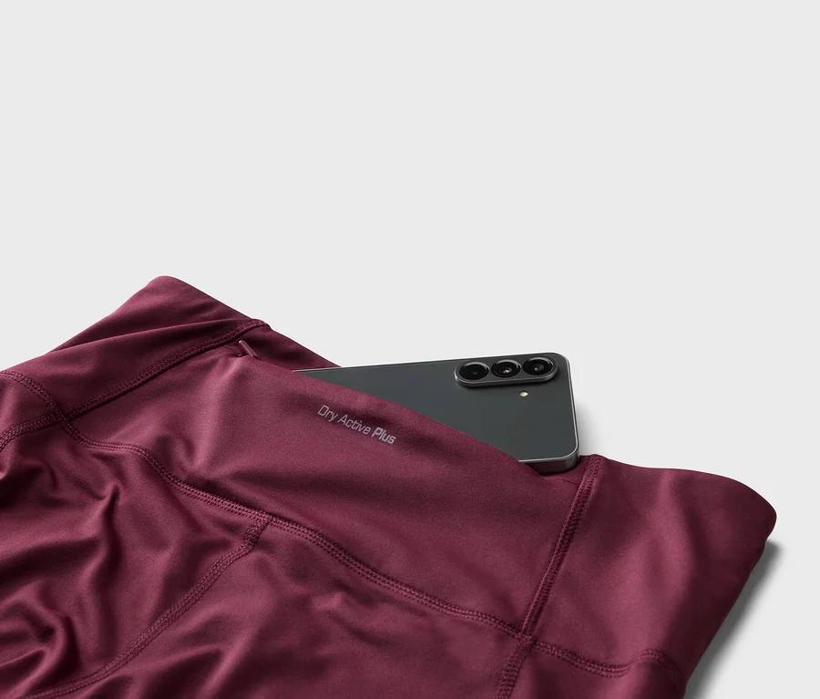Bordó színű leggings közelképe „Dry Active Plus” felirattal és egy fekete okostelefonnal a zsebében.