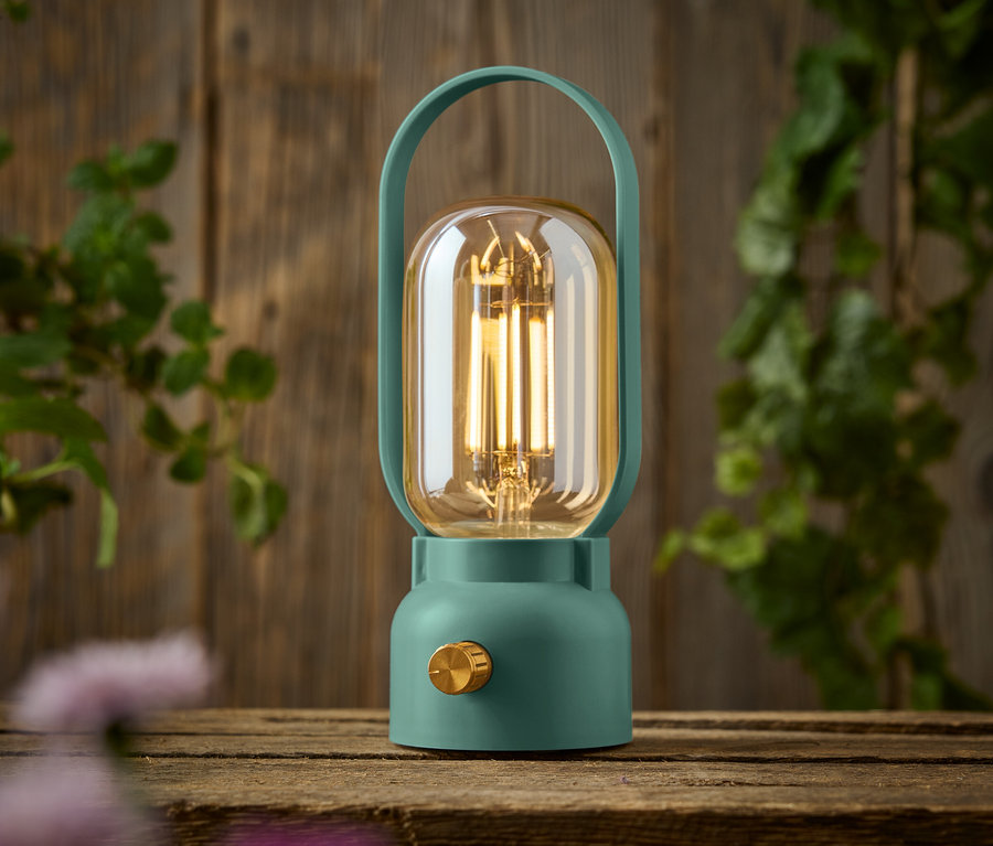 Egy zöld lámpa arany gombbal egy fa asztalon áll.