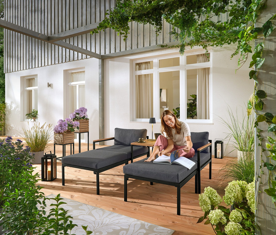 Egy nő ül egy szürke kerti ágyon és könyvet olvas. A háttérben két „Elin” növényoszlop látható.