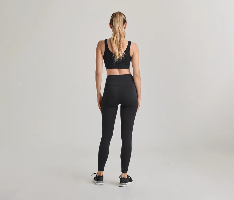 Hátulról látható nő, fekete sportmelltartót, fekete magas derekú leggingset és fekete sportcipőt visel. Szőke haja lófarokban van.