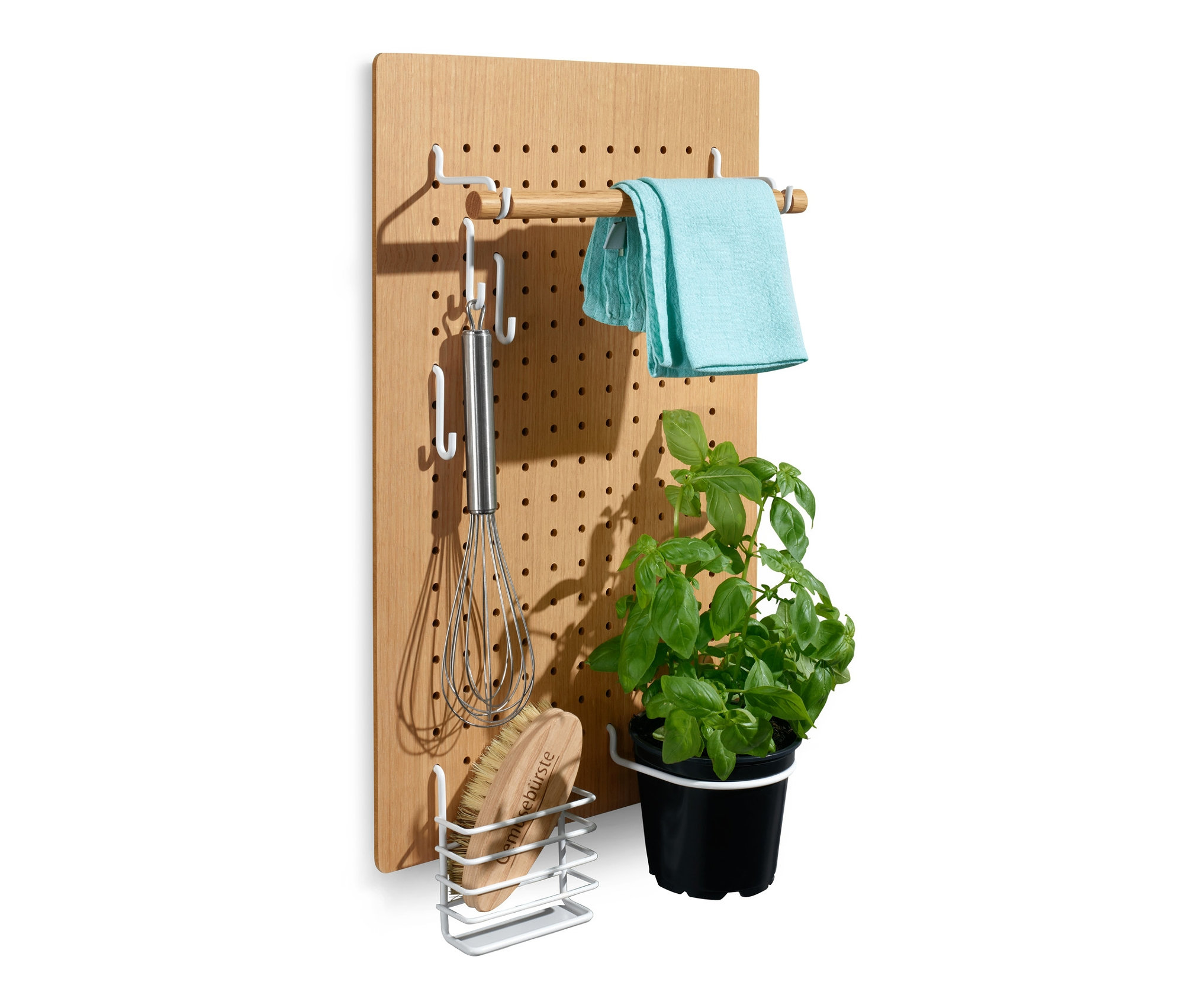 Lyukacsos falitábla, kiegészítő tárolókkal, rajta törlőkendő, habverő, kefe és egy cserepes növény.