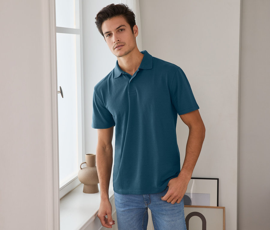 Férfi pózol az ablaknál, sötétkék funkcionális pólóingben.