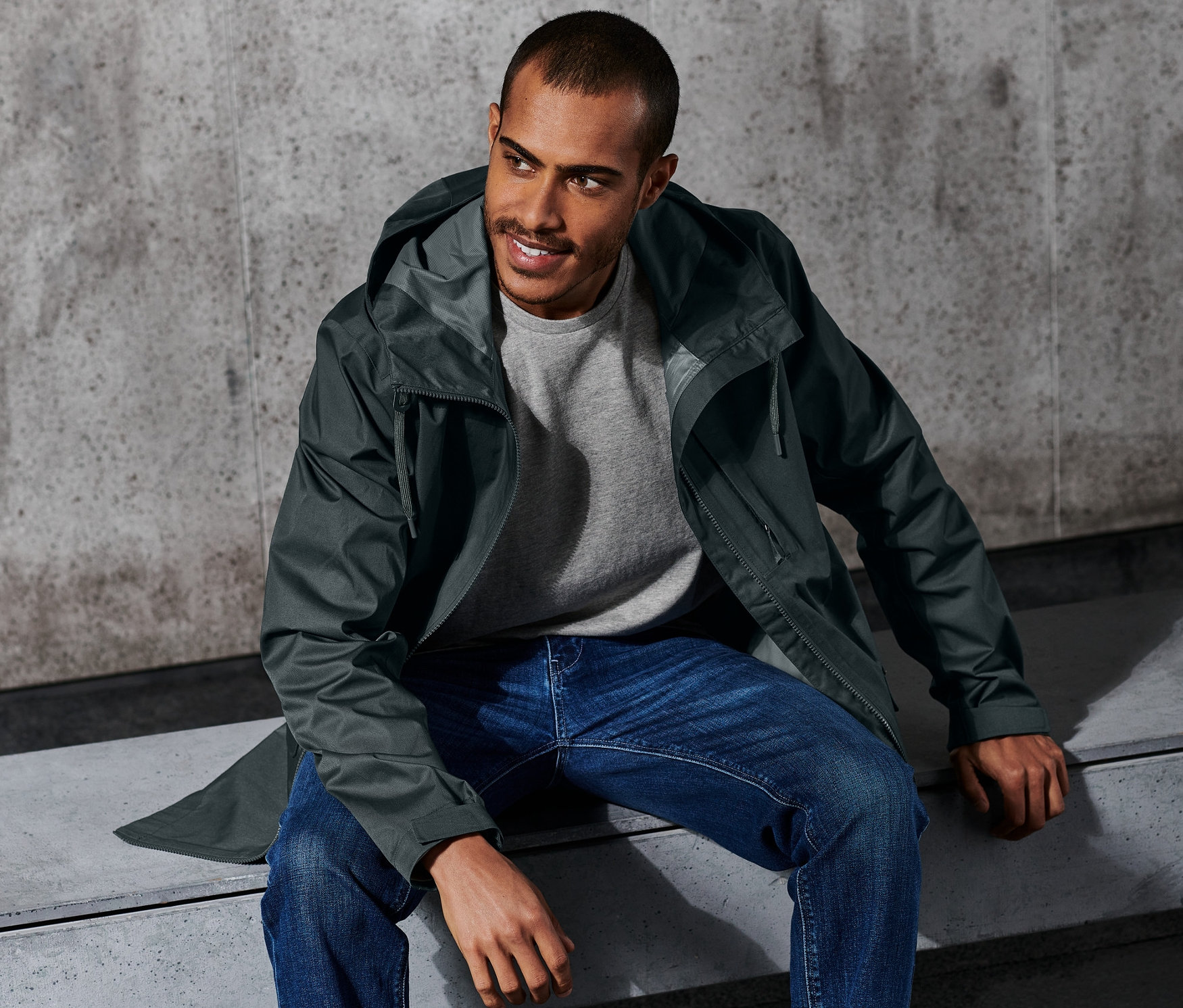 Férfi ül a padon, zöld funkcionális dzsekit visel.