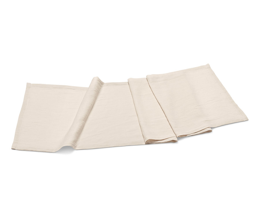 Egy bézs muszlin asztali futó összehajtva fekszik egy fehér háttéren.