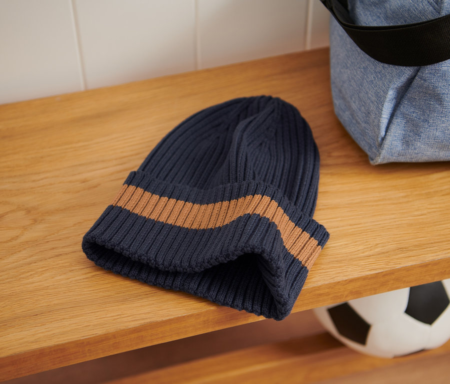 A fa polcon egy Gyerek kötött sapka, sötétkék/barna és egy sporttáska fekszik.