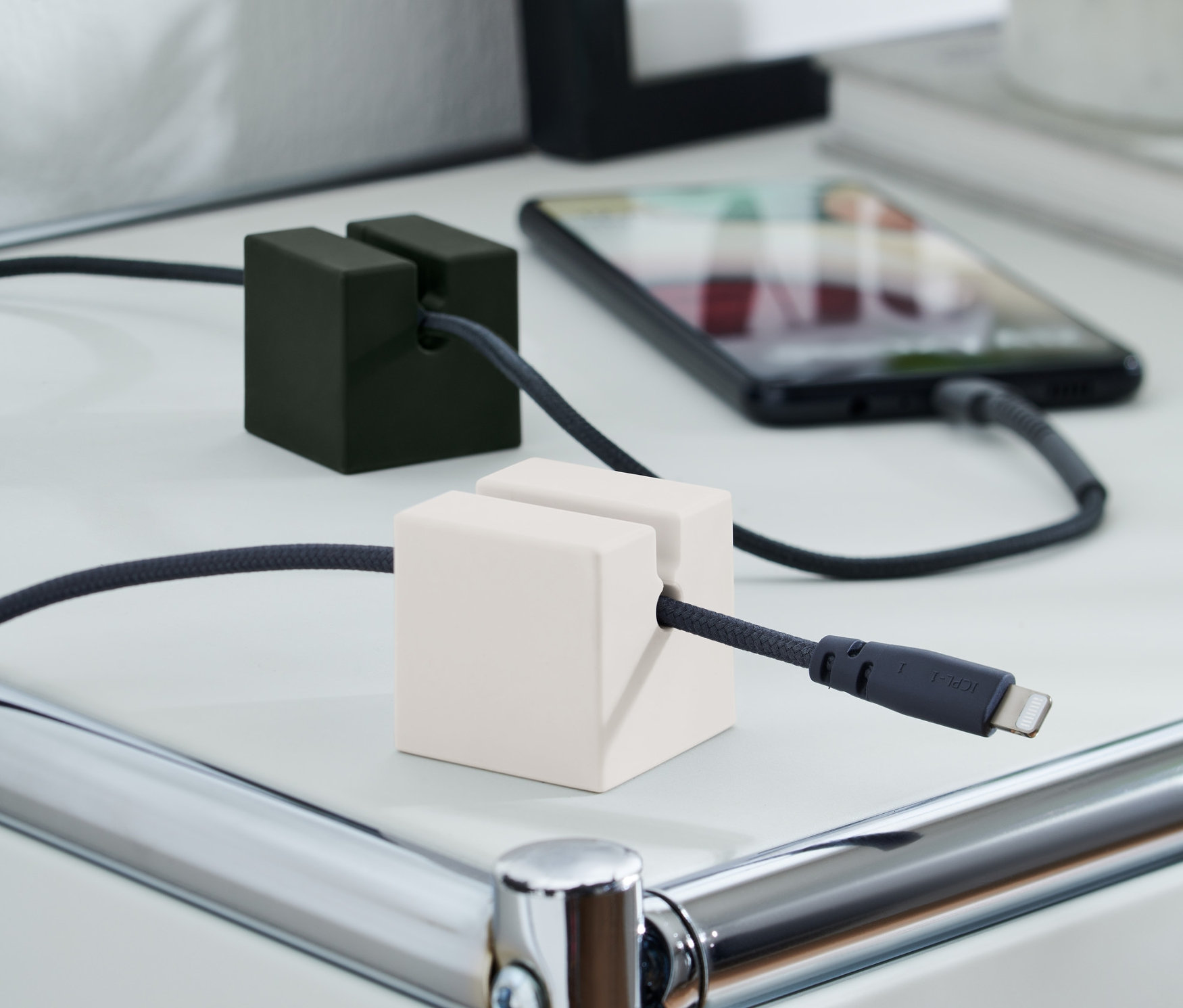 Egy 2 kábelrendszerező tartja a töltőkábeleket egy fehér asztalon. Az egyik fekete, a másik fehér.