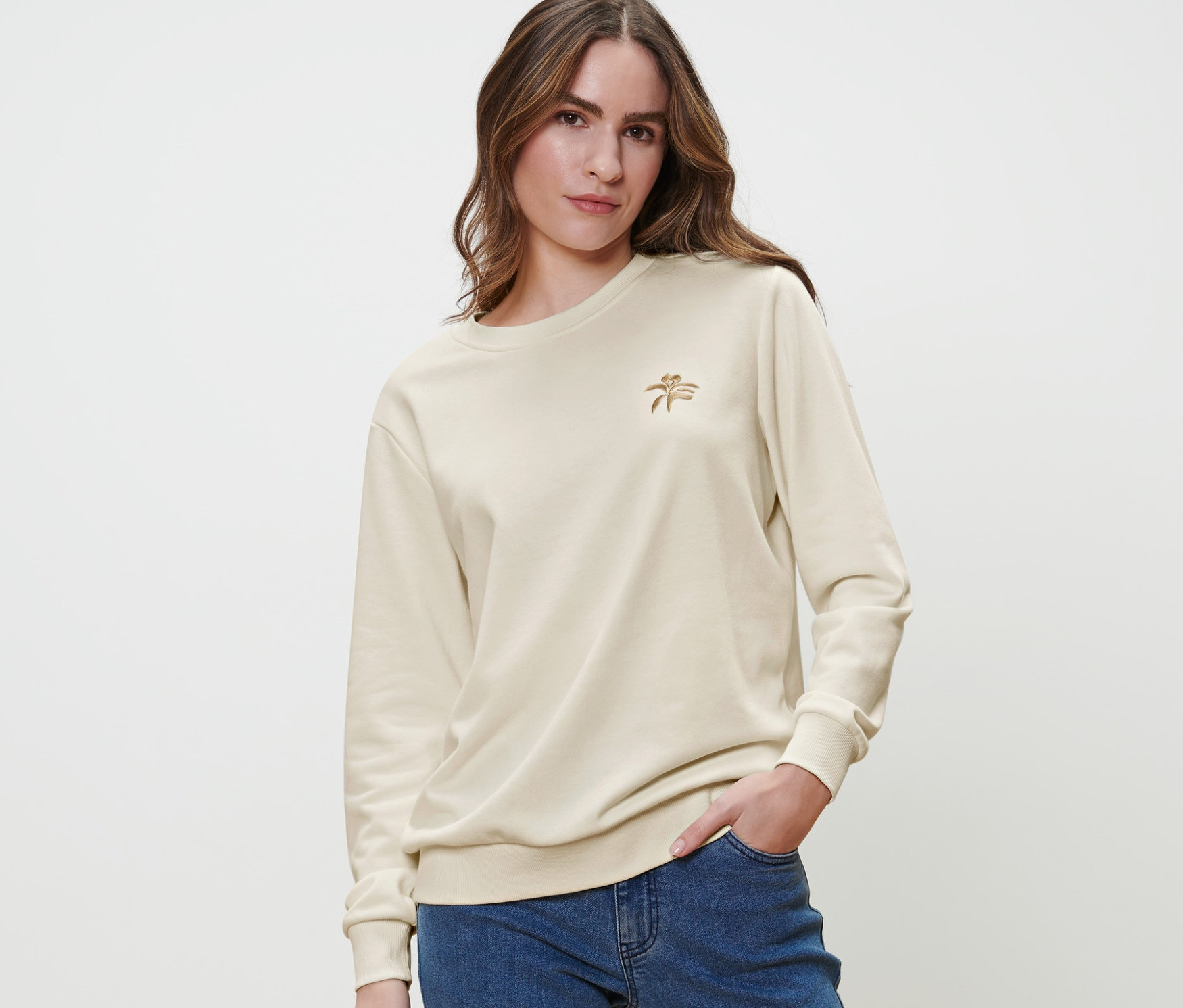 Nő krém színű, hímzett szabadidőfelsőben és kék farmerben pózol.