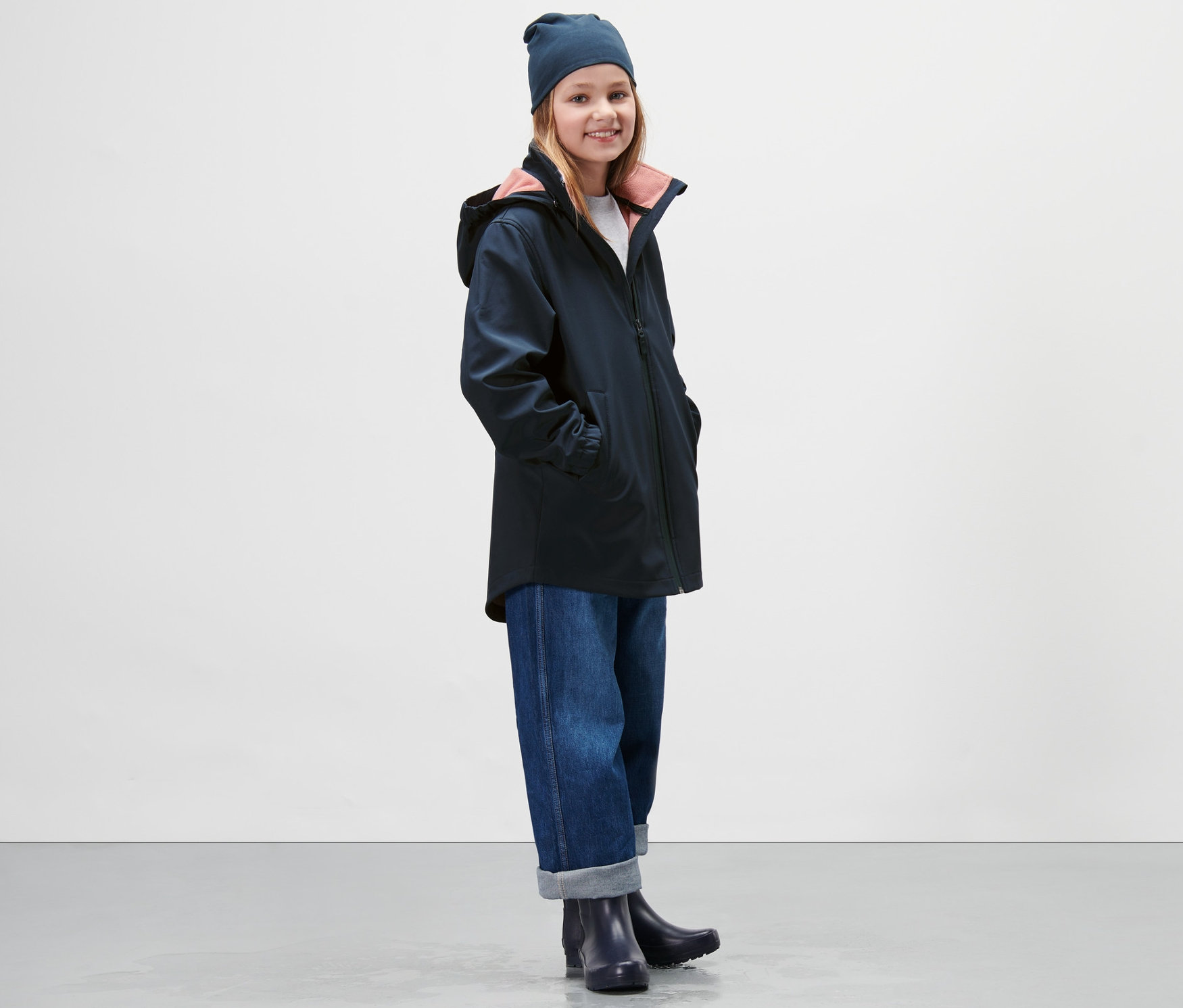 Lány sötétkék softshell kabátot, farmert és sapkát visel.