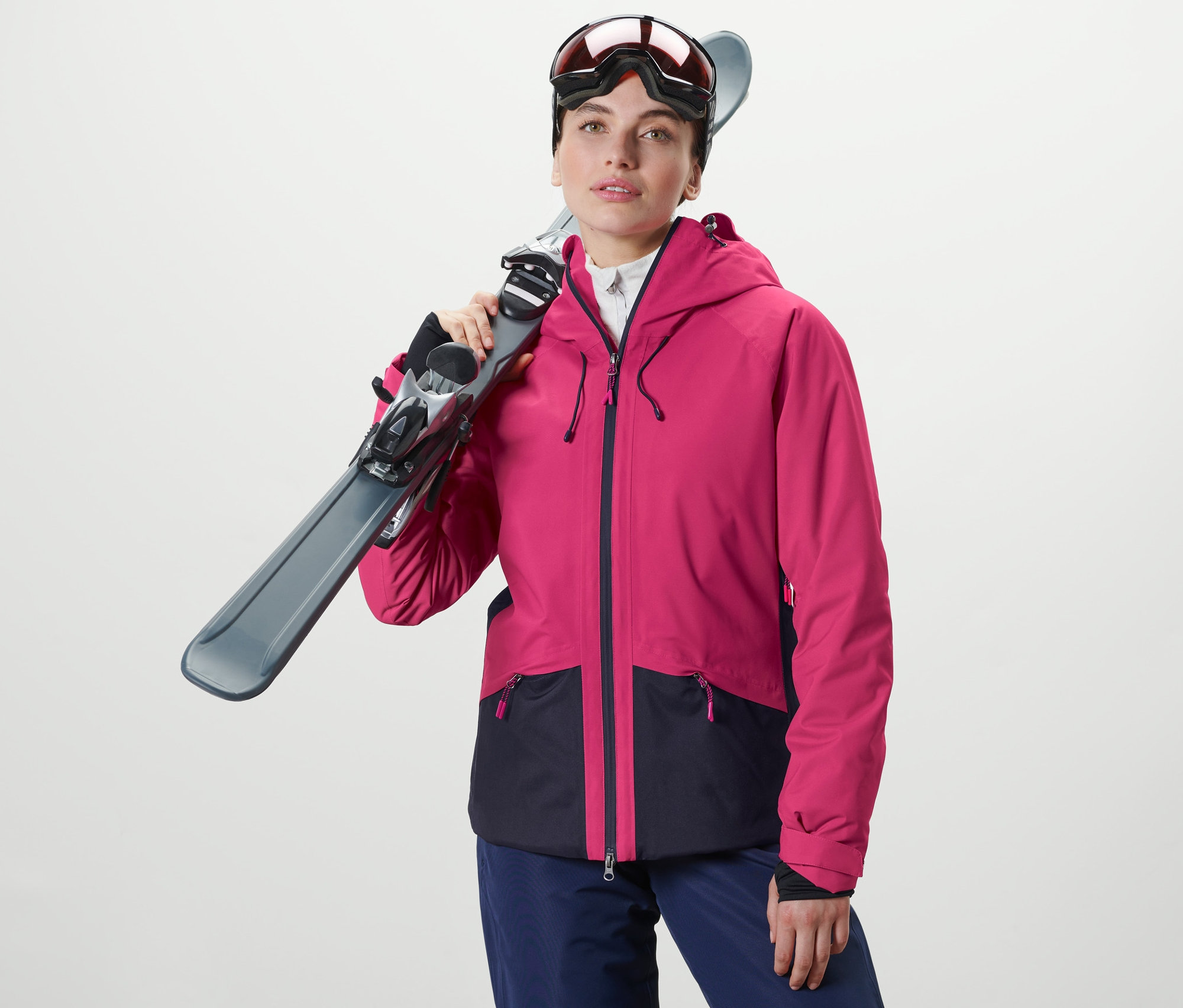 Nő tartja a sílécet a vállán. Női síkabátot visel, pink/sötétkék színben.