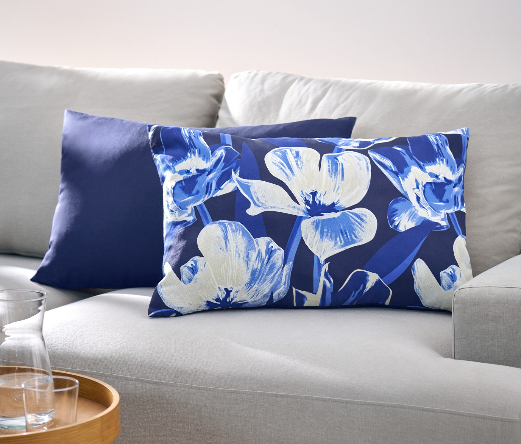 Egy világosszürke kanapén két díszpárnahuzat látható, az egyik sötétkék, a másik virágmintás.