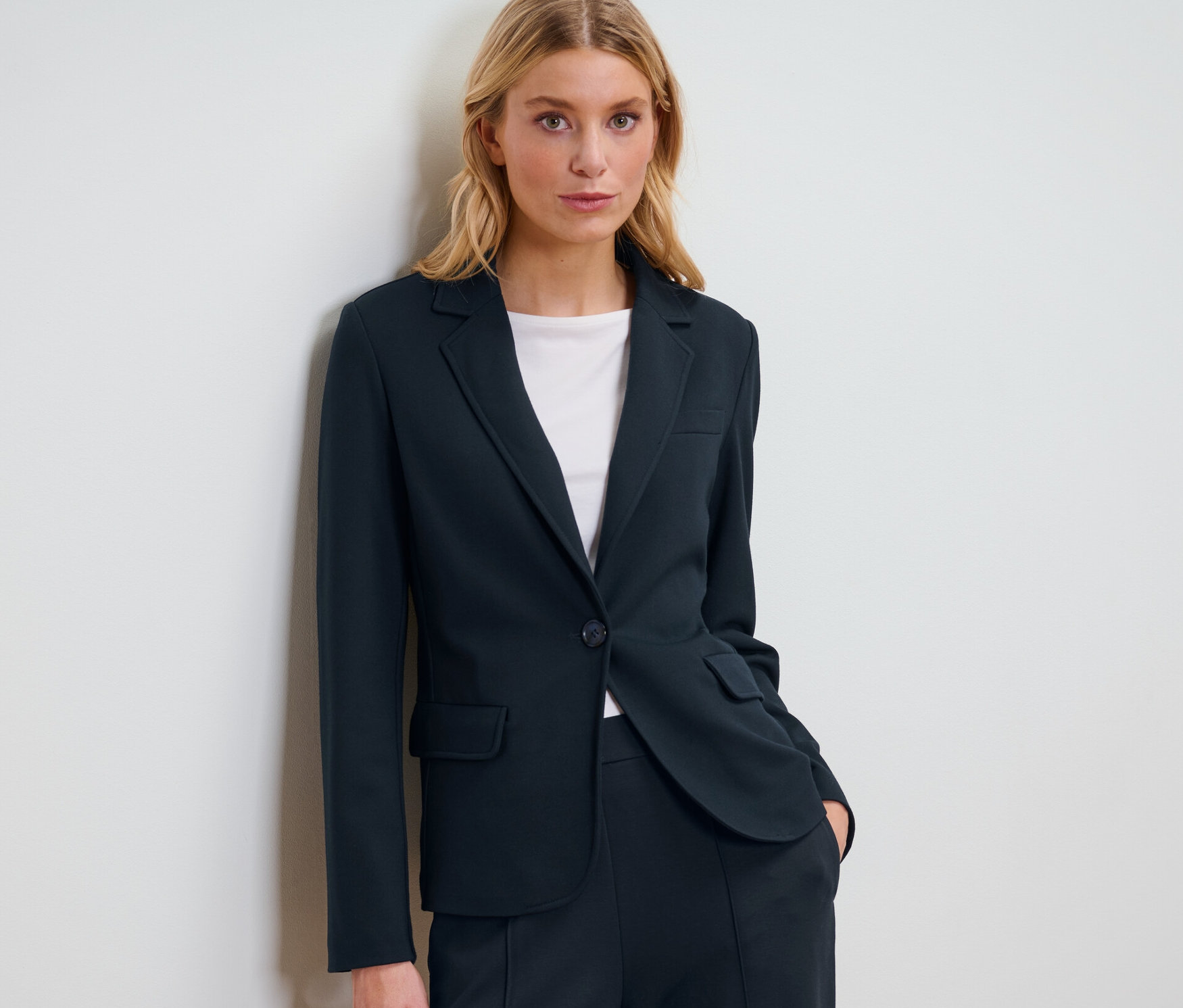Egy szőke nő sötétkék jersey blézerben pózol.