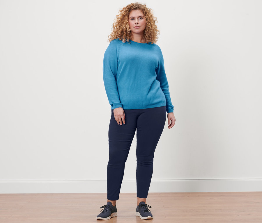 Nő áll sötétkék sztreccsnadrágban és kék kötött pulóverben.