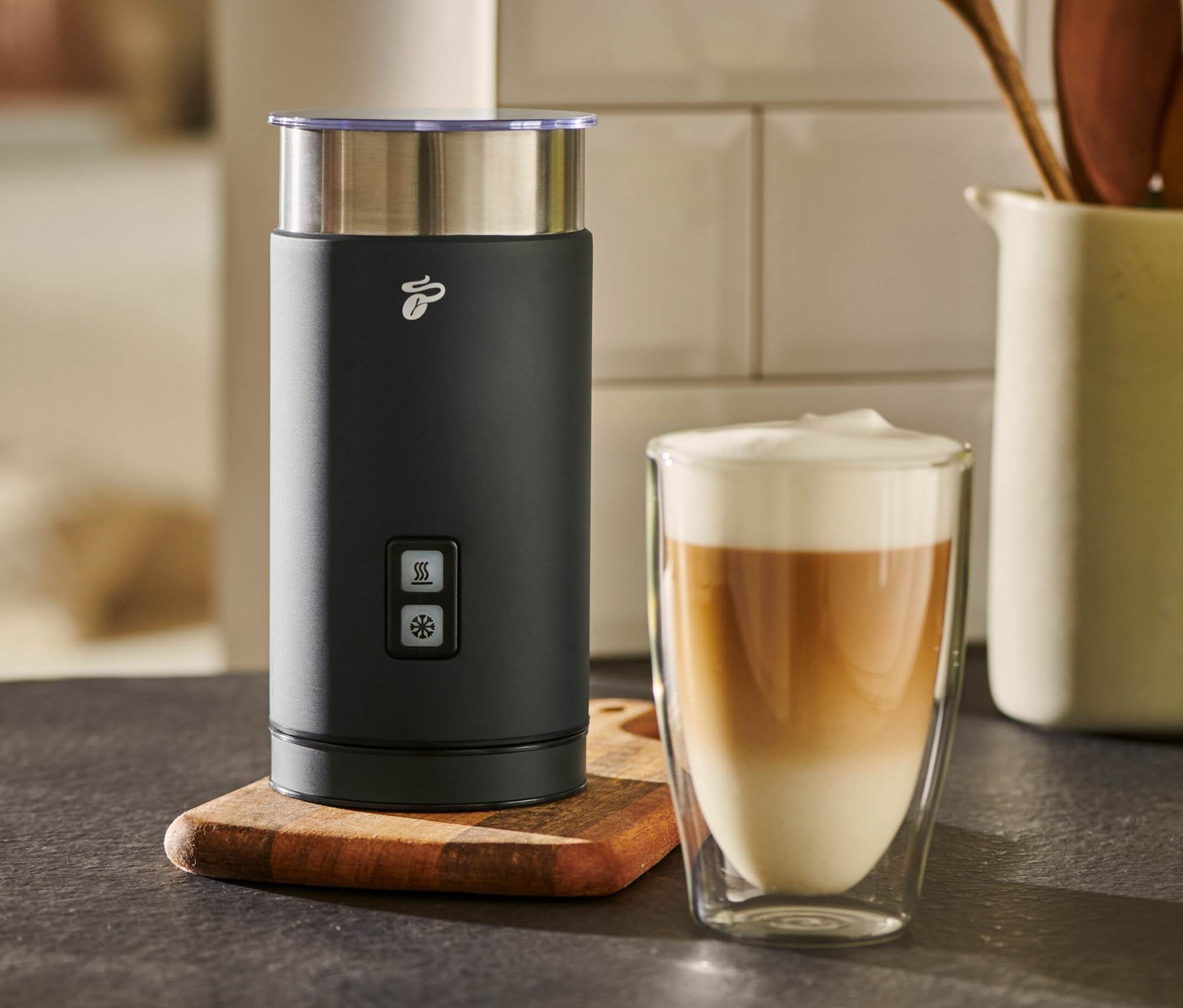Egy fekete elektromos tejhabosító áll egy pohár tejeskávé mellett.