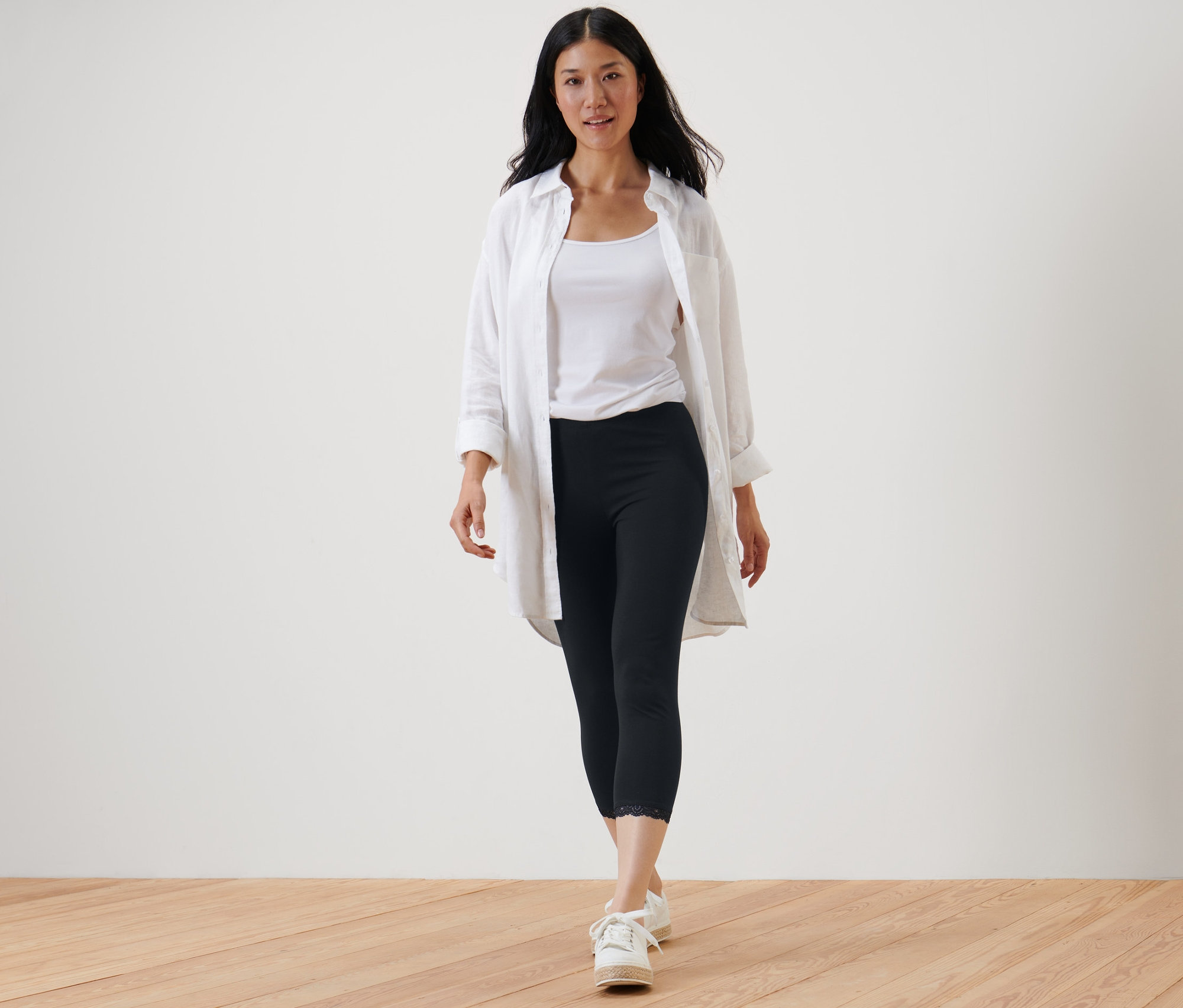 Egy nő sétál, fekete, 3/4-es, csipkés szegélyű leggingset, fehér trikót és fehér inget visel.