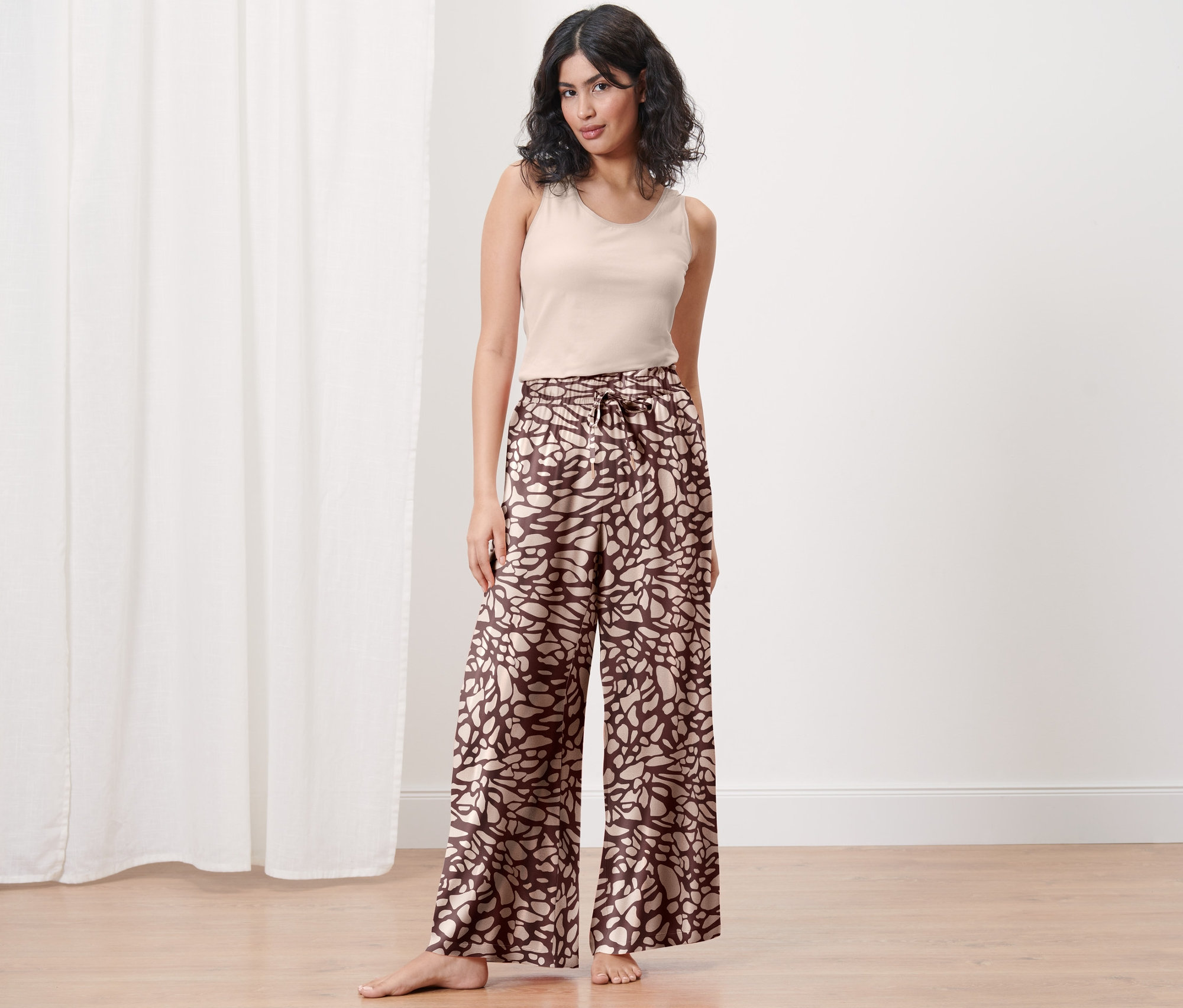 Egy nő áll, mintás női bőszárú szabadidőnadrágot és trikót visel.