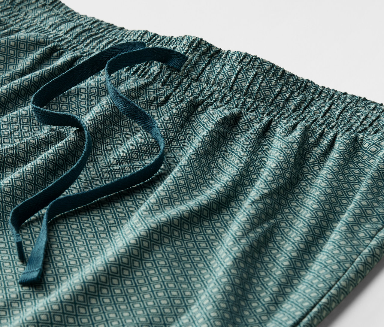 Egy zöld, mintás pizsamanadrág részlete, elasztikus derékpánttal és húzózsinórral.