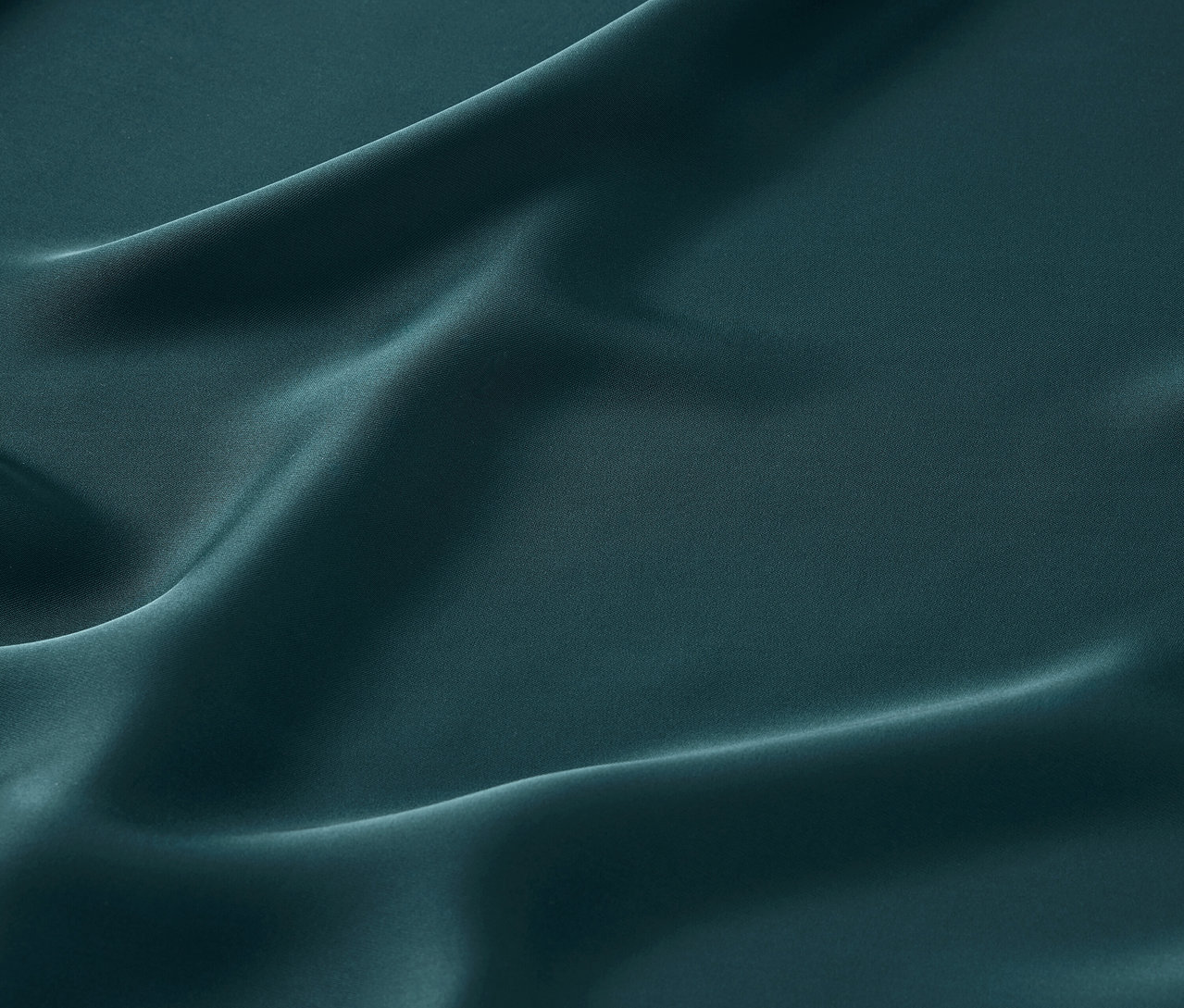 Közeli kép egy smaragdzöld szatén anyagról lágy redőkkel.