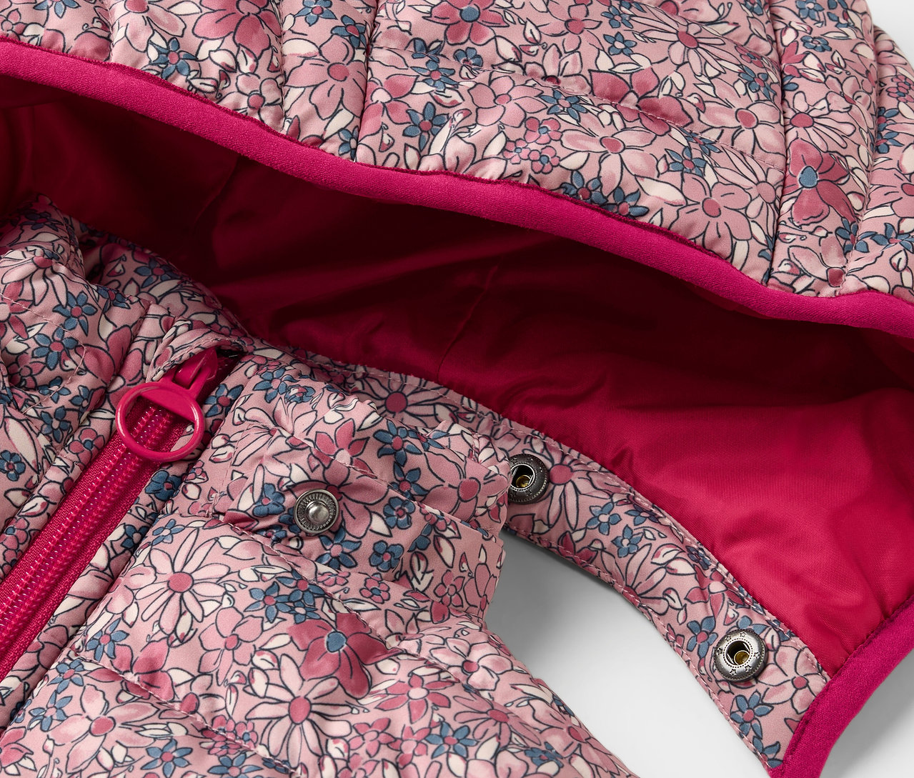 Egy virágmintás, steppelt gyerekkabát részlete, cipzárral és patentokkal.