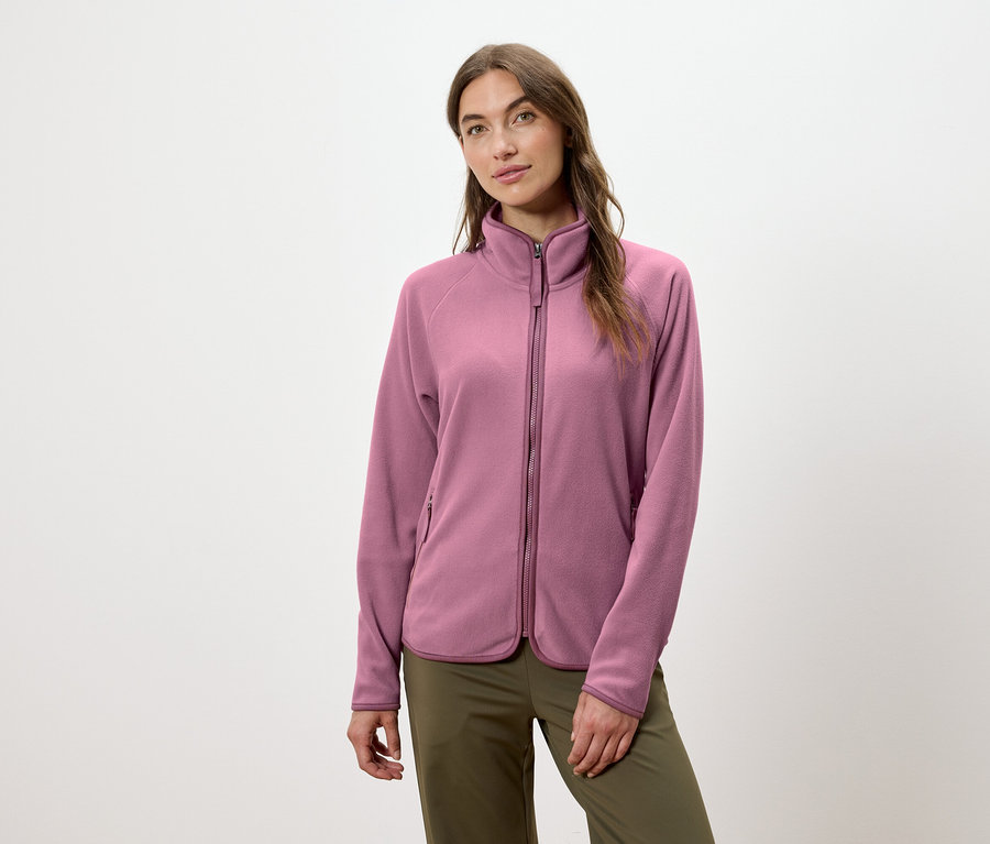 Egy nő rózsaszín cipzáras polárkabátot és zöld nadrágot visel.