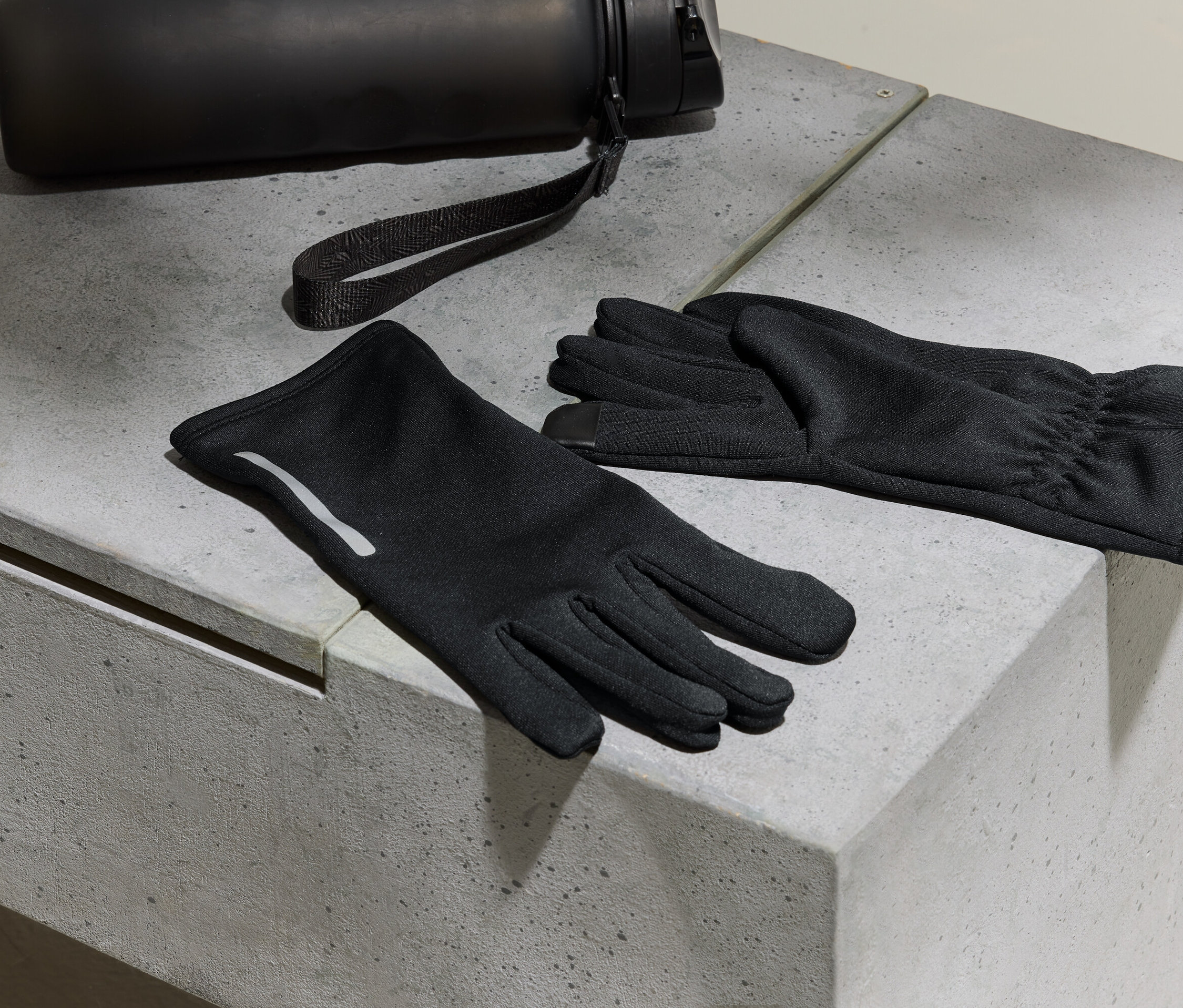 Fekete kesztyűk és egy vizes palack fekszik egy beton felületen.