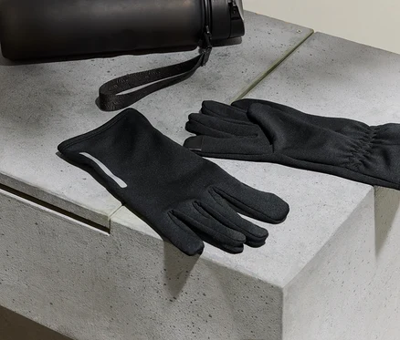Fekete kesztyűk és egy vizes palack fekszik egy beton felületen.