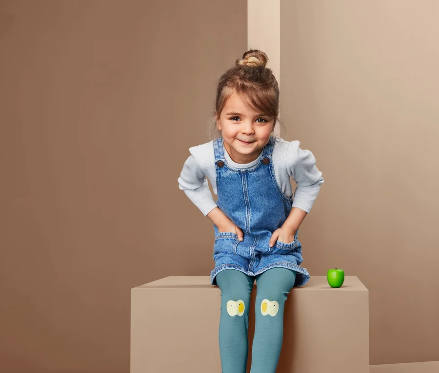 Egy kislány ül farmerruhában és 2 leggings szettben, foltokkal.