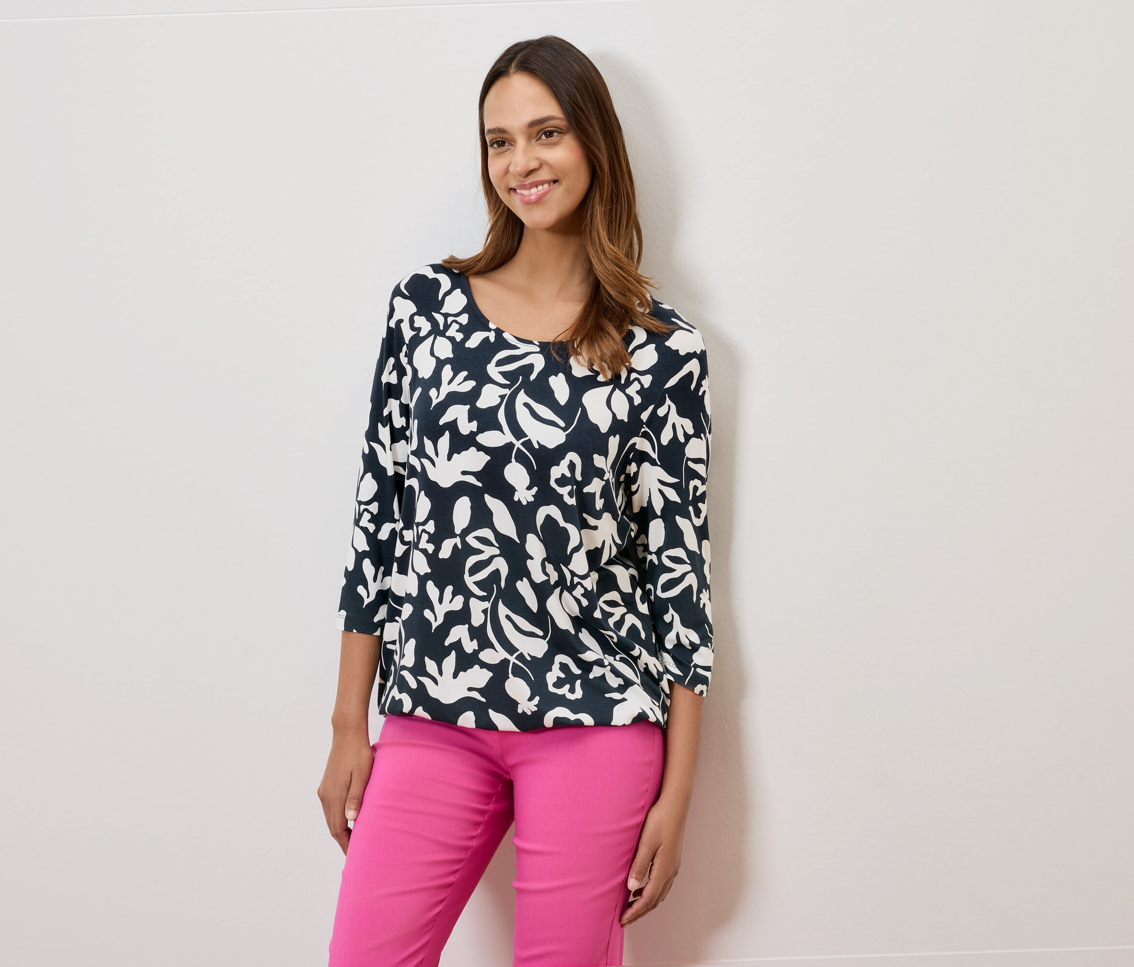 Nő virágmintás sötétkék blúzt és rózsaszín nadrágot visel.