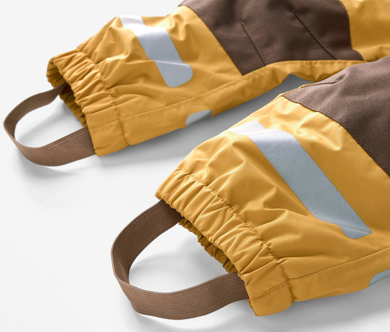 Egy eső elleni kezeslábas részlete barna és sárga színblokkokkal, valamint rugalmas lábpántokkal.