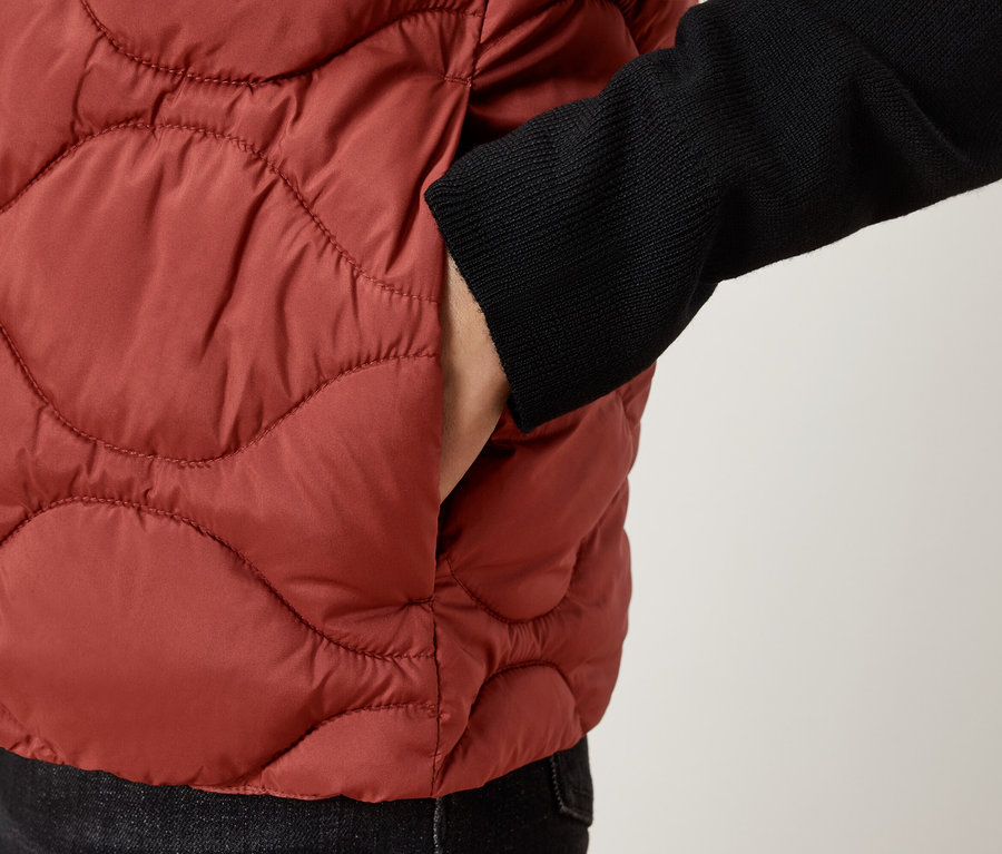 Közelkép egy személyről, aki barna, steppelt mellényt visel, kezével a zsebében.