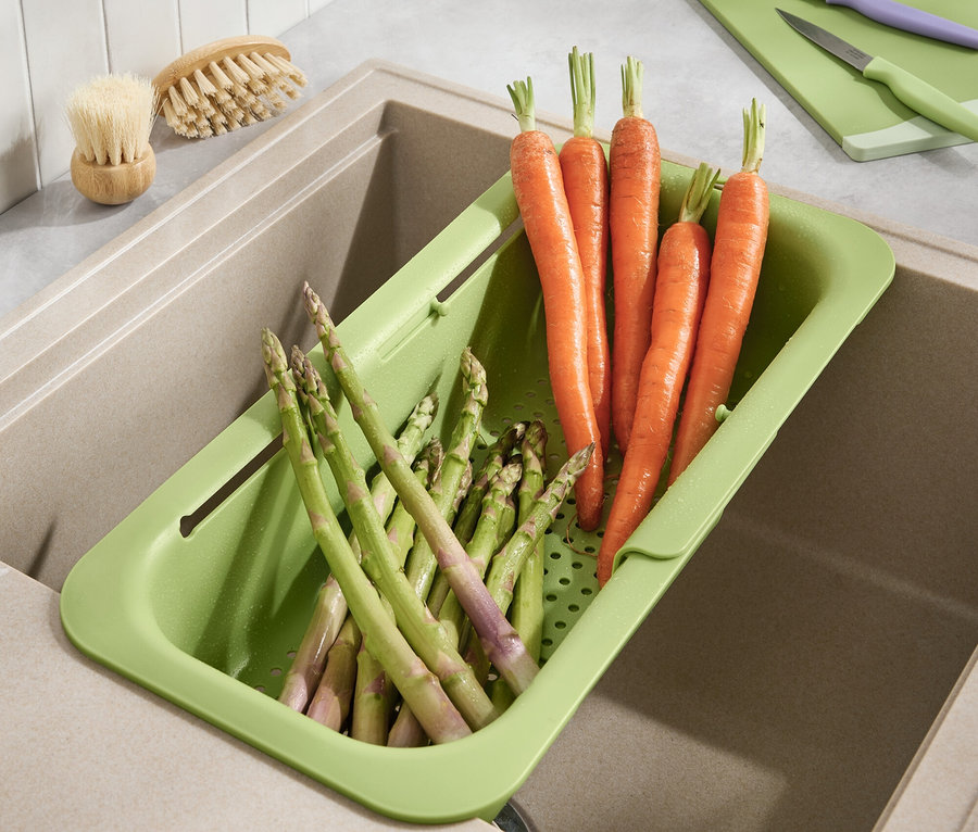 Sárgarépák és spárga fekszik egy zöld csepegtetőben a mosogatóban.