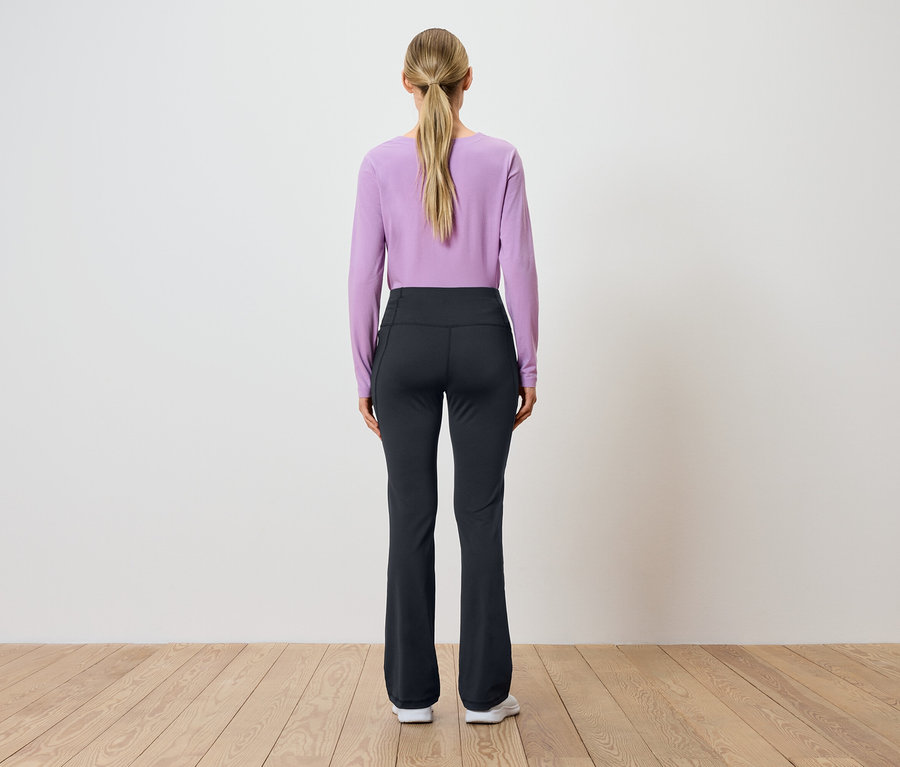 Hátulról látható egy lófarokba kötött szőke hajú nő, aki lila, hosszú ujjú felsőt és fekete nadrágot visel.