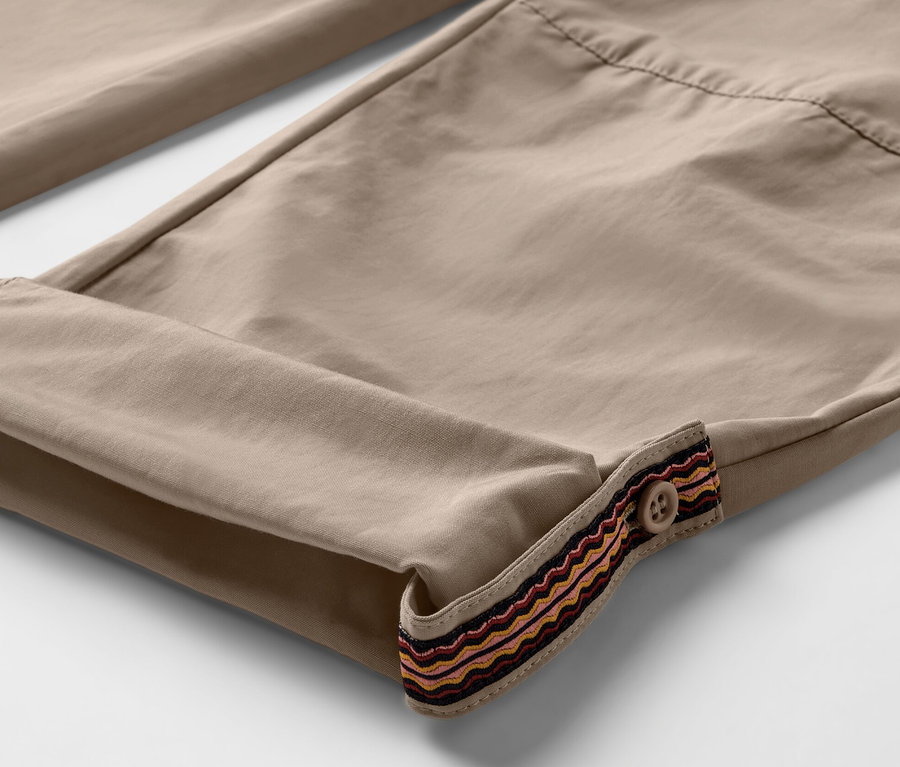 Egy bézs színű, felhajtott szárú, díszszegélyes és gombos outdoor nadrág részlete. A nadrág szúnyogok elleni védelemmel van ellátva.