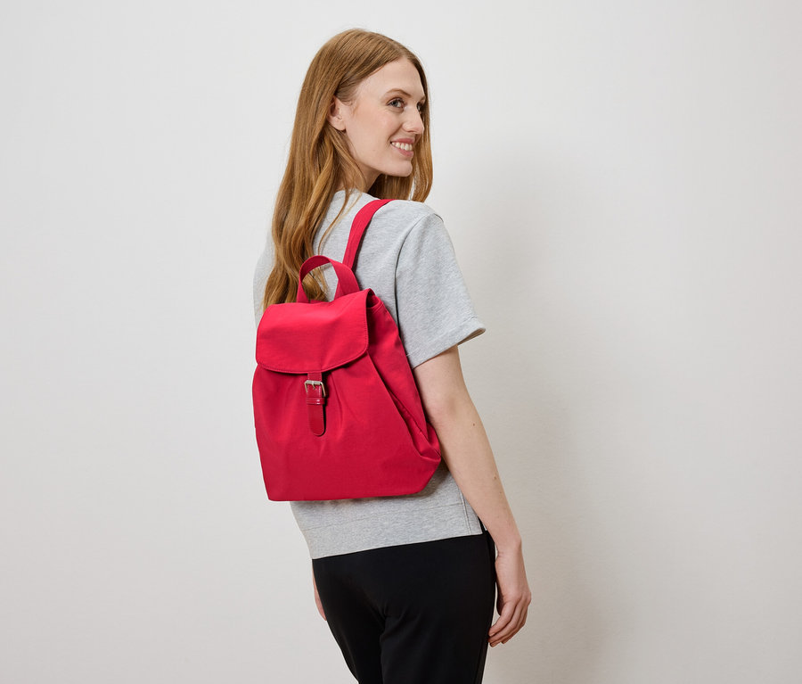 Nő piros hátizsákkal a hátán, balra néz.