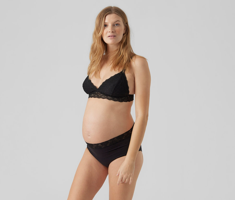 Egy várandós nő fekete csipkés bralette-et és 2 db MAMALICIOUS kismama magasderekú alsót visel.