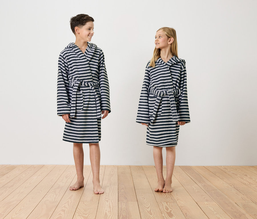 Egy fiú és egy lány mezítláb állnak egy fapadlón, csíkos, kapucnis köntösben.