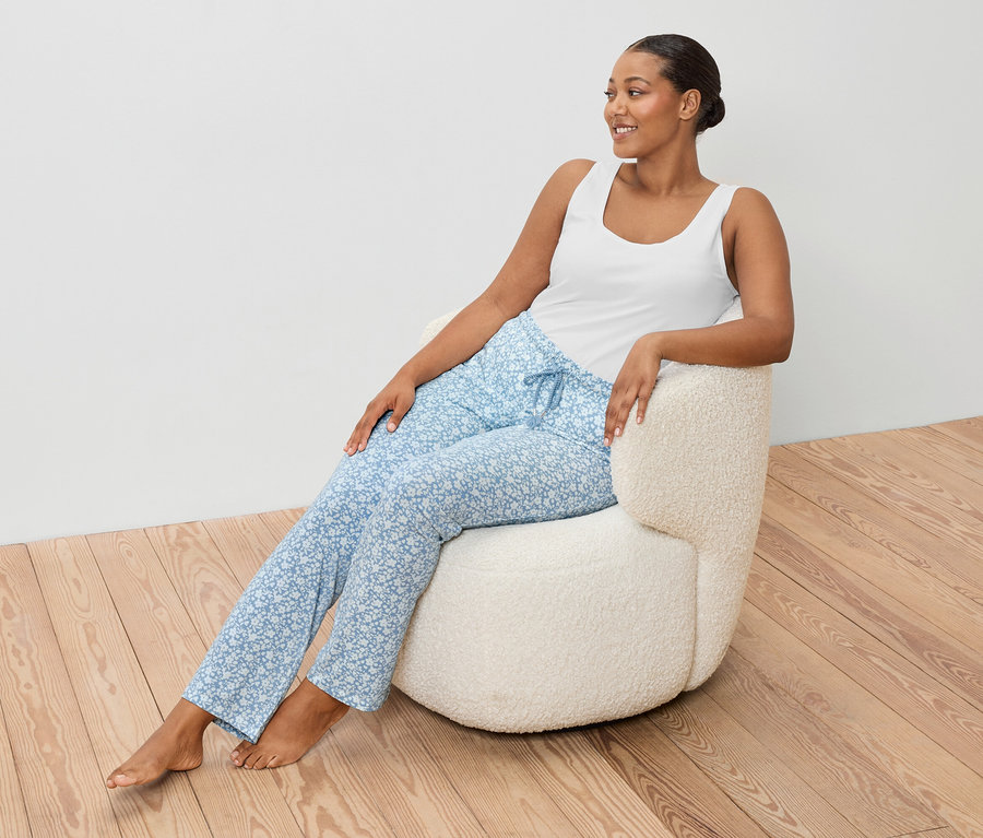 Nő ül egy fotelben, fehér trikót és kék nadrágot visel.