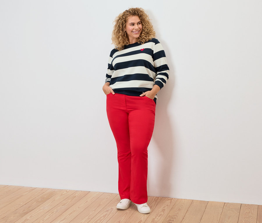 Göndör hajú nő csíkos felsőt és piros nadrágot visel.