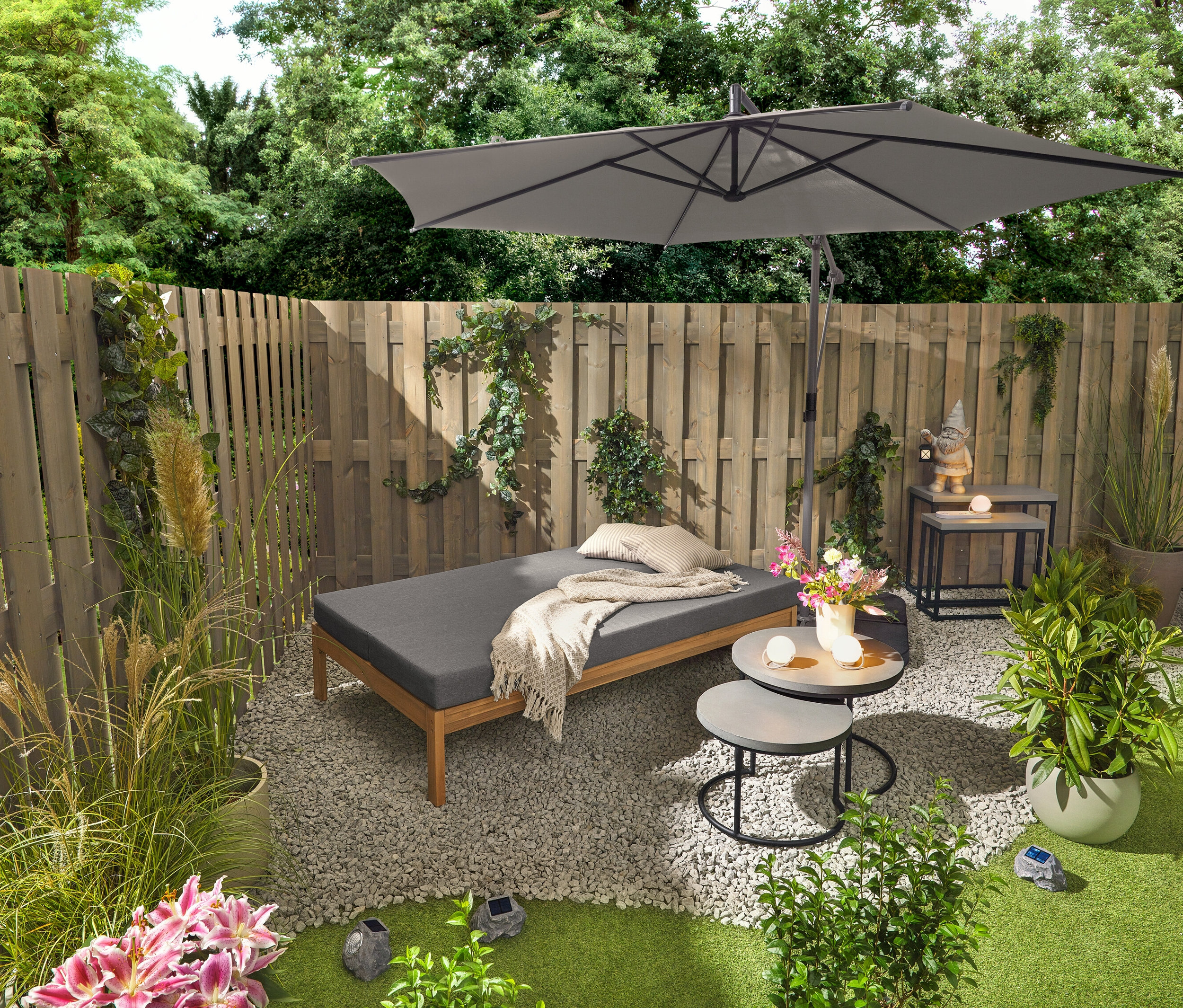 Egy 2 az 1-ben kerti pad, amely dupla napozóágyként funkcionál, két polycement asztallapos kerti asztal mellett áll (kb. 50 cm és 60 cm átmérőjű). Egy LED lámpás kerti törpe a 2 polycement asztallapos kerti konzolasztal egyikén áll. Három akkumulátoros asztali lámpa és három napelemes LED-es kő is látható.