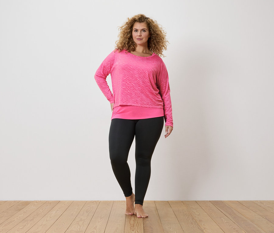 Göndör hajú nő rózsaszín, zebracsíkos hosszú ujjú felsőben és fekete leggingsben.