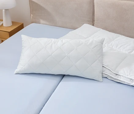 Egy fehér Cell Solution® párna, 80 x 40 cm-es méretben, egy kék ágyon fekszik egy fehér paplan mellett.