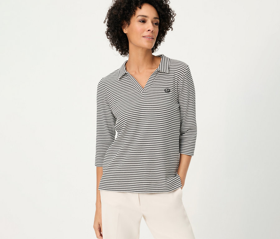 Nő visel háromnegyedes ujjú, csíkos Olsen pólóinget és világos nadrágot.