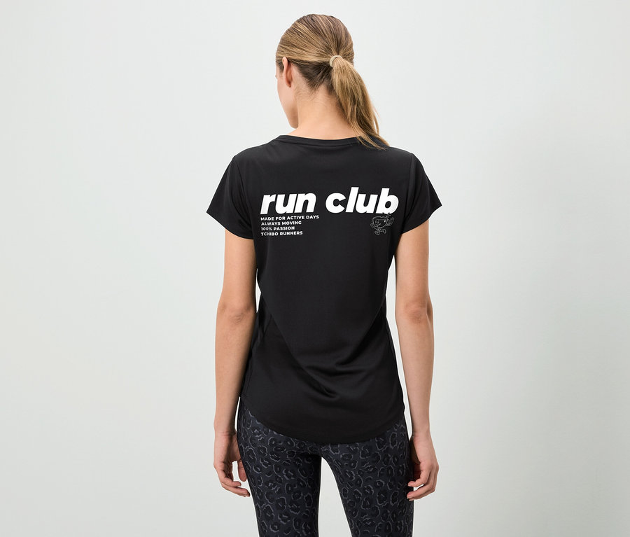 Hátulnézet egy fekete "run club" feliratú pólót és mintás leggingset viselő, lófarokba kötött hajú nőről.
