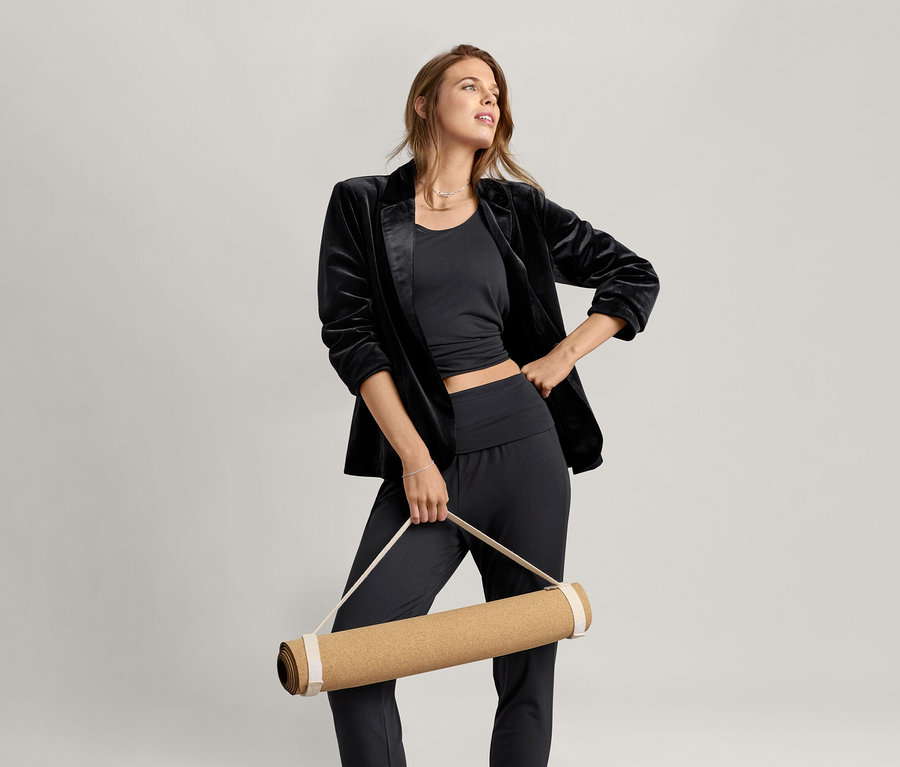 Nő visel egy fekete 2 az 1-ben sportfelsőt és egy jógamatracot tart.