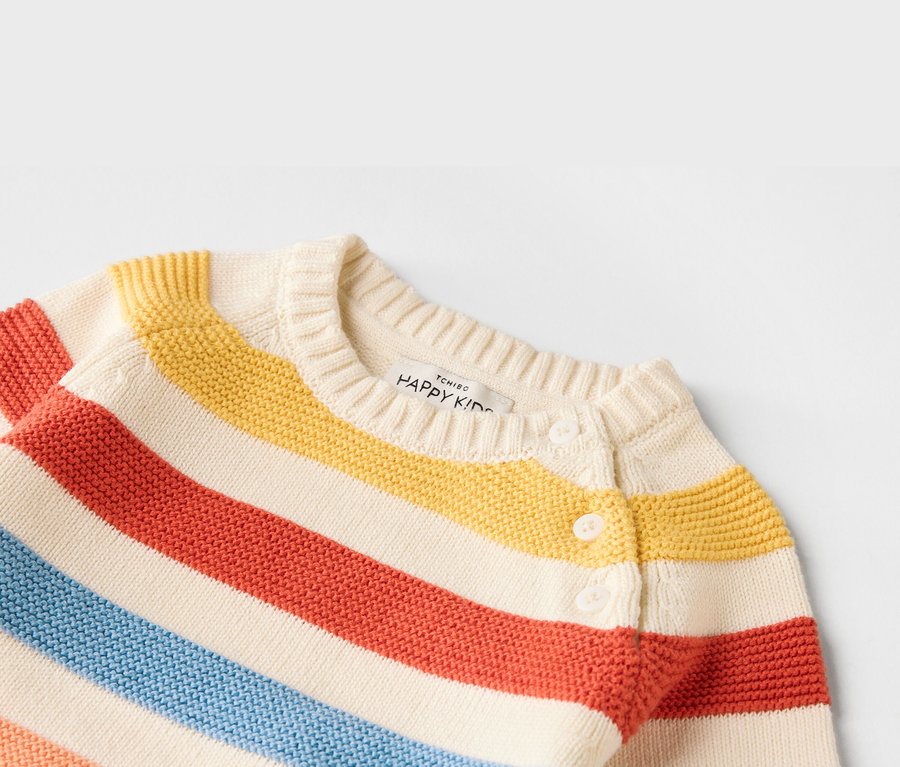 Közeli kép egy piros, sárga és kék csíkos, gombos kötött gyerek kardigánról, fehér gombokkal.