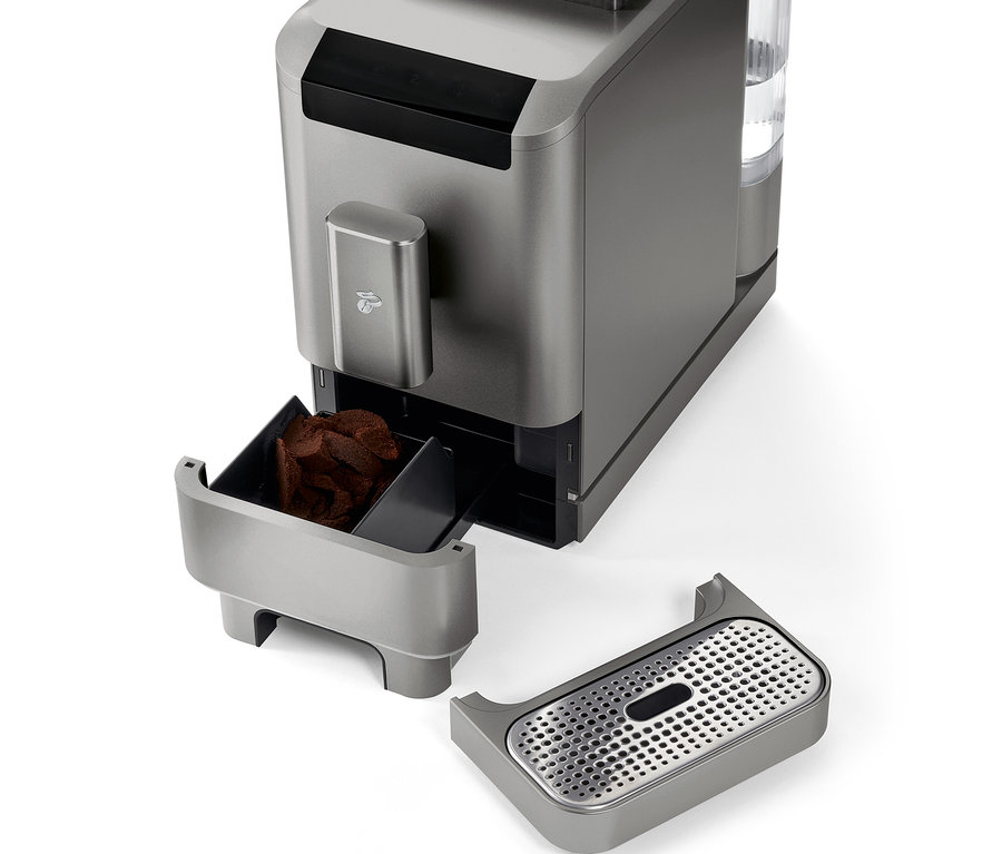 Közelkép a »Esperto2 Caffè« automata kávéfőzőről Titanium Silver színben, eltávolított kávézacc-tartállyal és csepptálcával.