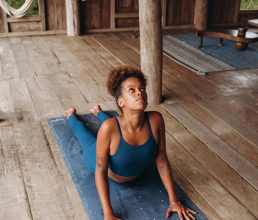 Fiatal nő jógázik kék szettben, kék, fehér pöttyös szőnyegen.