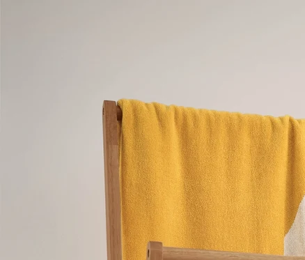 Egy sárga-fehér csíkos jacquard fürdőlepedő és 3 csíkos, bézs törölköző lóg egy összecsukható fa ruhaállványon. Alatta 2 fonott tárolókosár található.