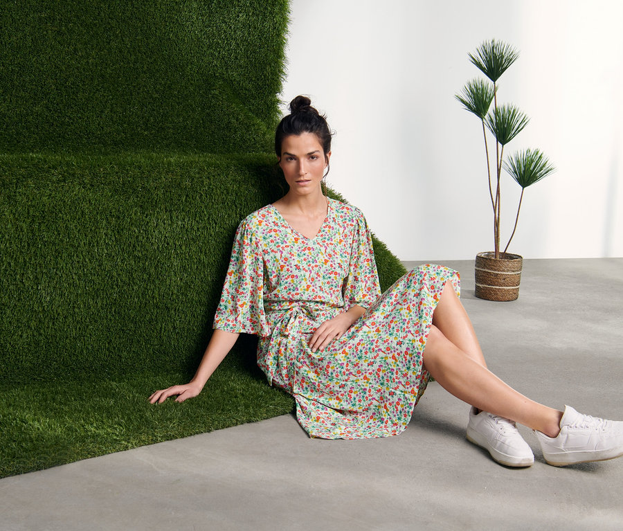 Nő ül a padlón egy zöld fal mellett, mintás ruhát visel.