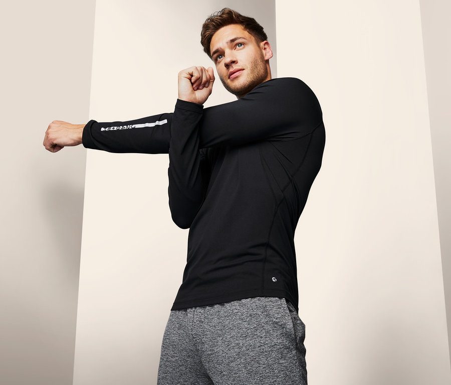 Férfi nyújtja a karját fekete funkcionális felsőben.